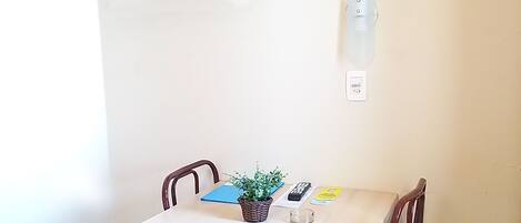 A small dining area with a table, chairs, a television mounted on the wall, and an air conditioning unit.