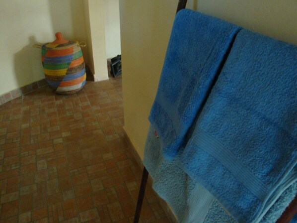 Une salle de bain avec une serviette bleue suspendue à un porte-serviettes, un panier coloré en fibres tressées et un sol carrelé.