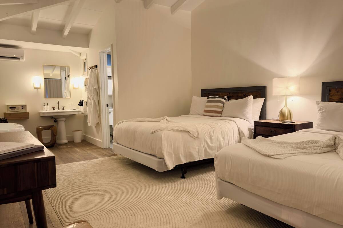 Een hotelkamer met twee bedden, een grote spiegel, een wastafel en een houten vloer.