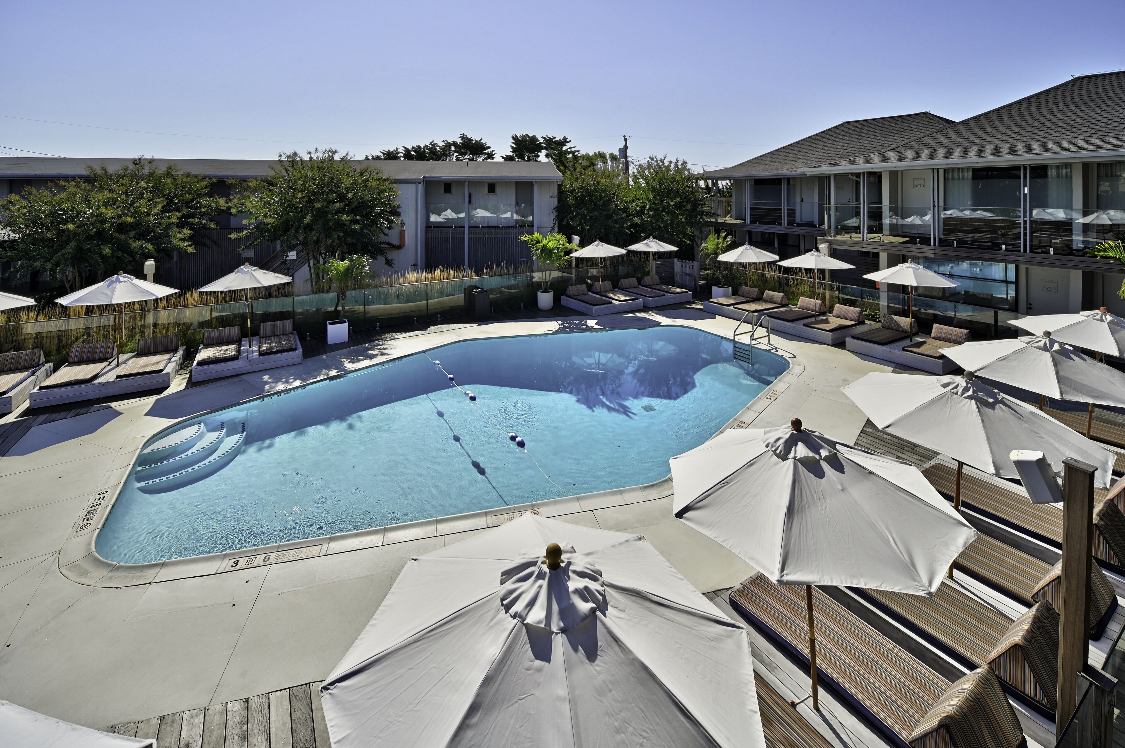 A swimming pool with lounge chairs and umbrellas, surrounded by a fence and trees.