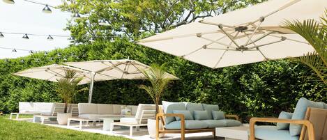 An outdoor seating area with white sofas, a wooden chair, and large umbrellas.