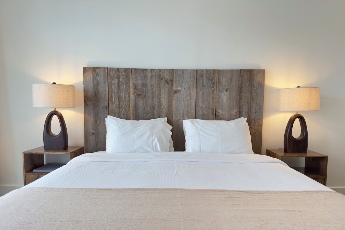 Een hotelkamer met een houten hoofdeinde, twee nachtkastjes met lampen, en een bed met witte lakens.