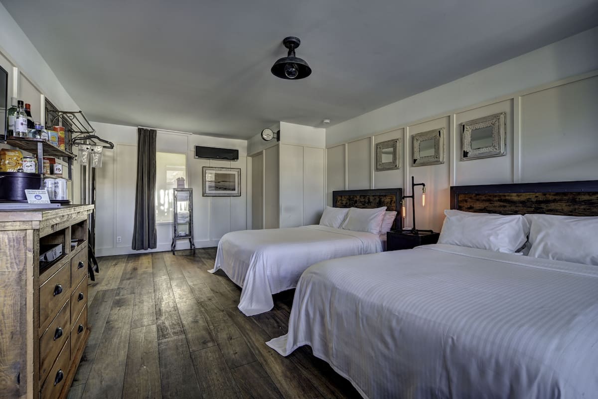 Een hotelkamer met twee bedden, houten vloeren, een dressoir en een plafondventilator.