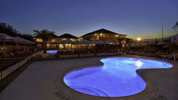 A swimming pool with a curved edge and a surrounding deck area with lounge chairs and umbrellas.