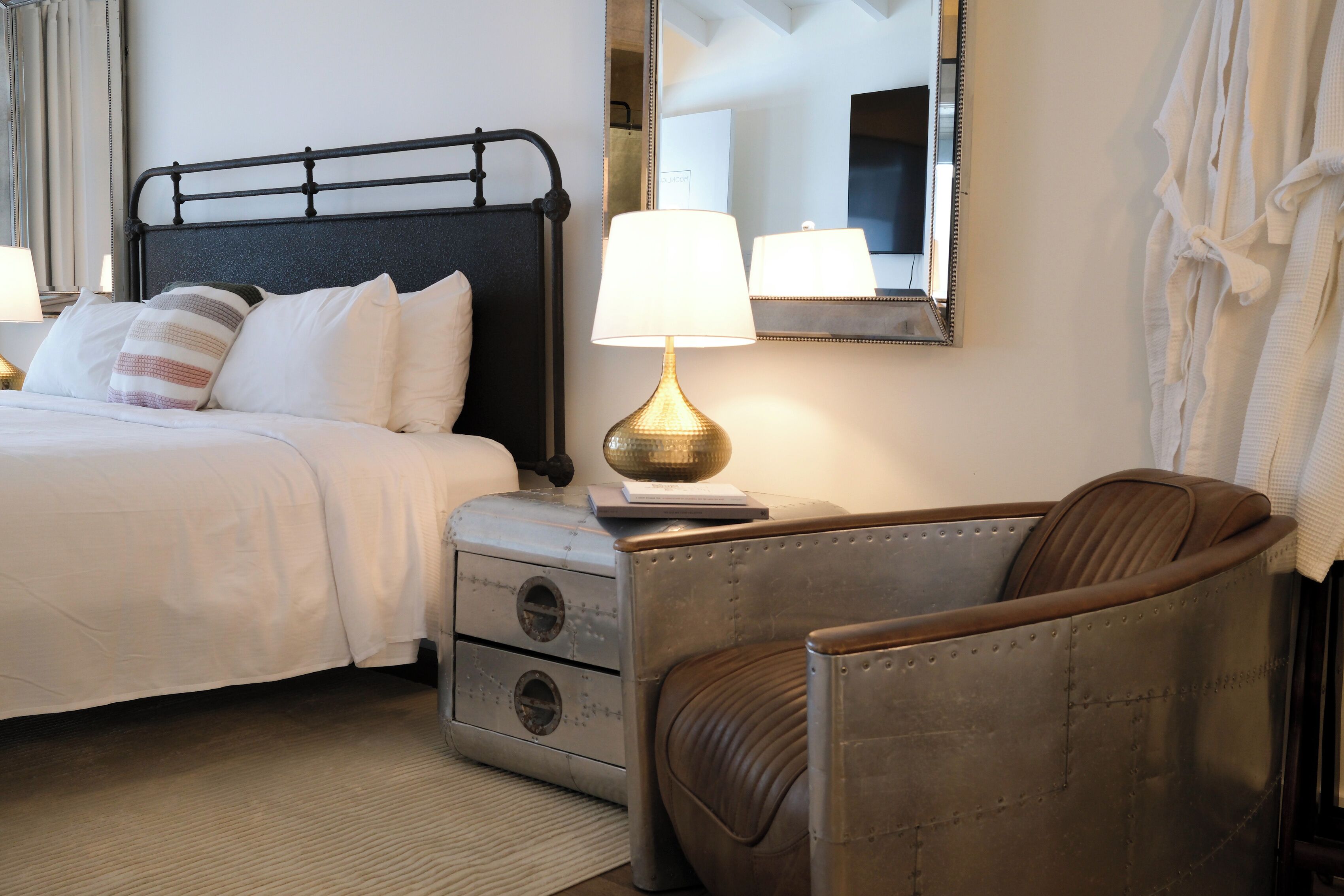 A hotel room with a bed, a nightstand, a lamp, a chair, and a mirror.