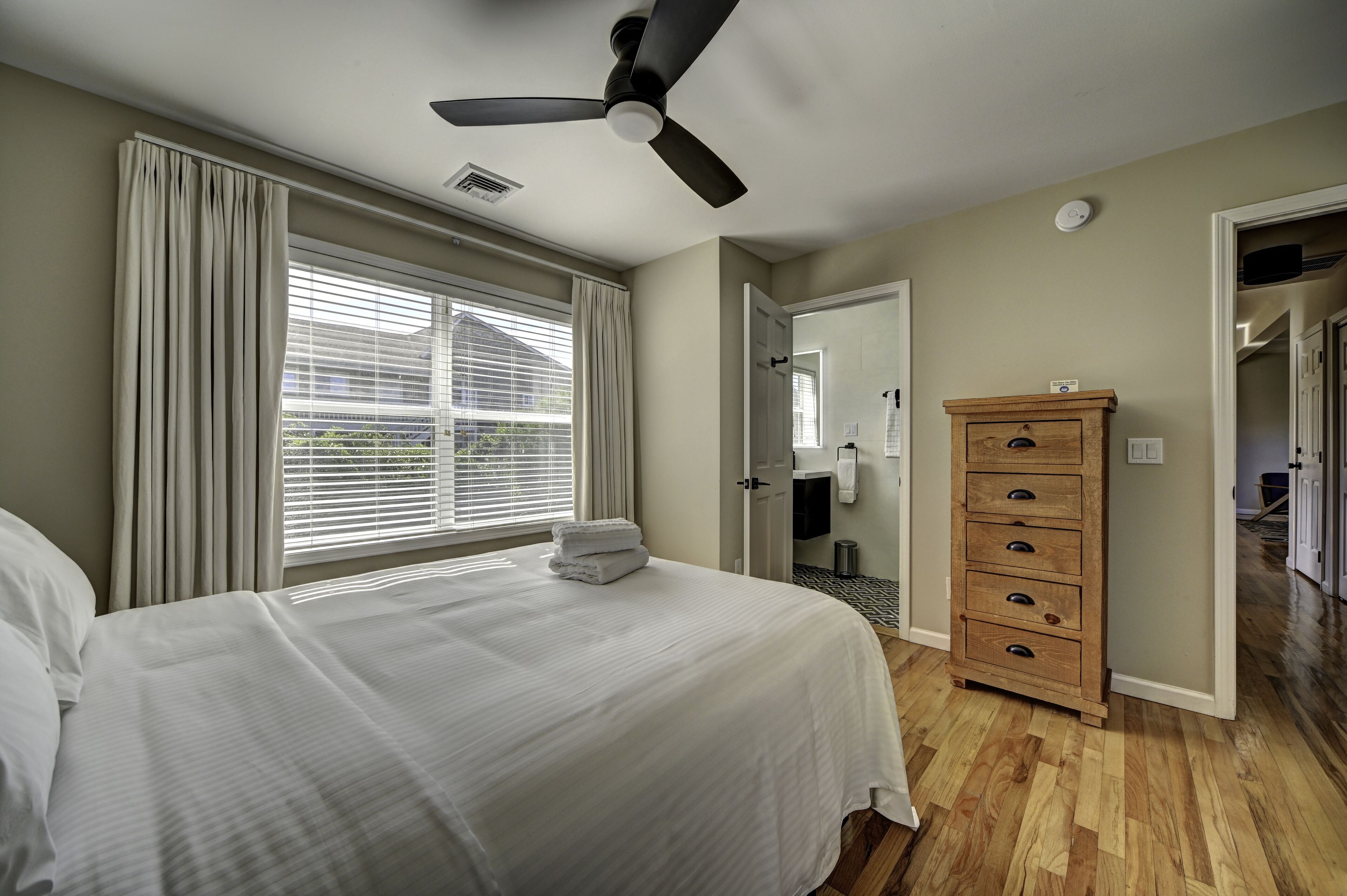 A bedroom with a bed, a ceiling fan, a wooden dresser, and a window with blinds.