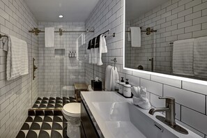 A modern bathroom with white subway tiles, a large mirror, a white sink with a modern faucet, and a toilet with a black and white patterned floor.