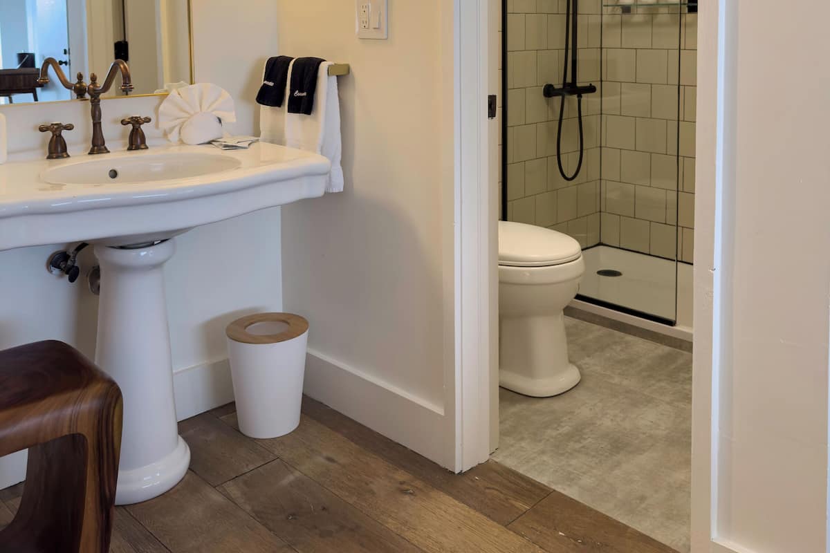 Een badkamer met een wastafel op voet, een spiegel, een handdoekhouder, een toilet en een douchecabine met glazen wanden.