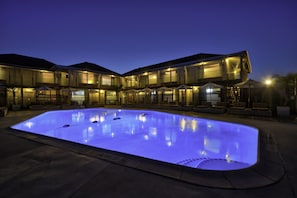 A swimming pool with a modern design, surrounded by a multi-story building with large windows and outdoor seating areas.