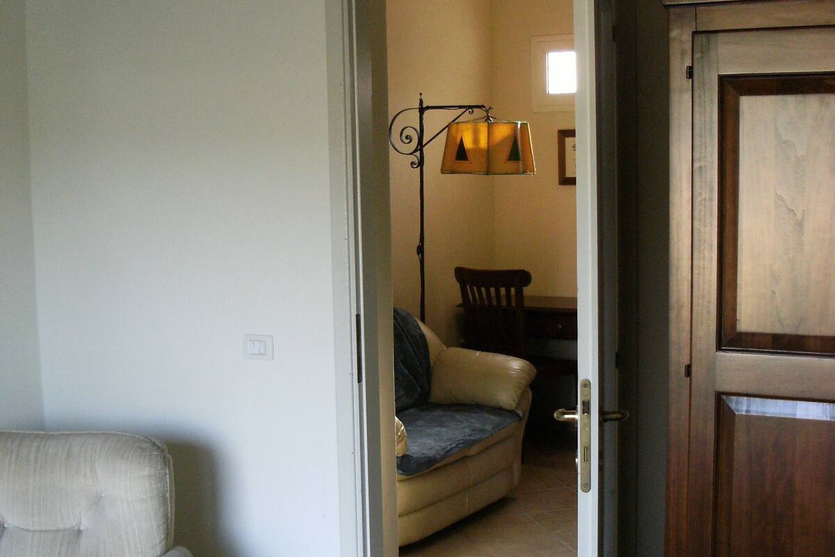 Een kamer met een bed, een stoel, een bank en een houten deur.