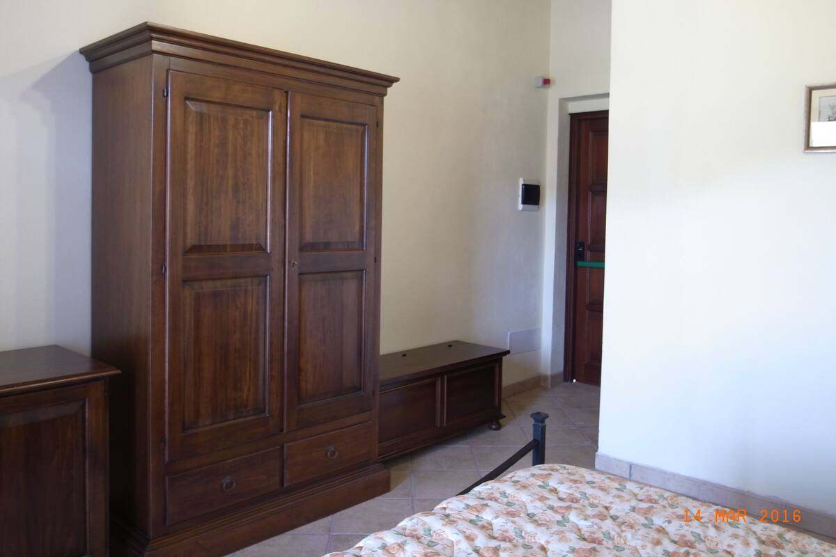 Een slaapkamer met een grote houten garderobe, een bed met bloemenbedrukking en een klein bankje.