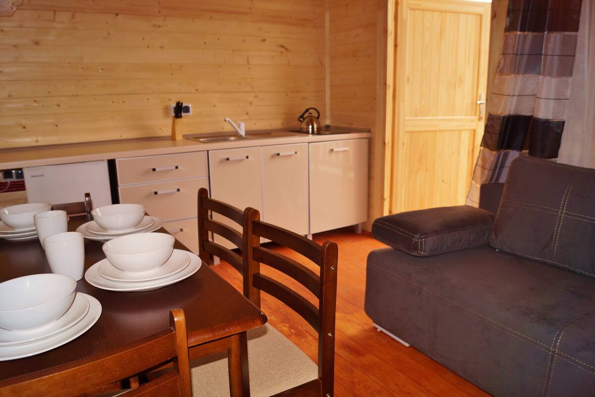 Un interior de madera con una mesa de comedor dispuesta con cuencos y platos blancos, un sofá y un mueble de madera.