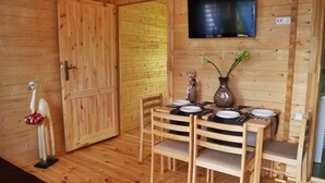 Un interior de madera con una mesa de comedor dispuesta para cuatro, un televisor montado en la pared y una puerta de madera.