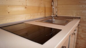 Una cocina con paredes de madera, un lavamanos de acero inoxidable y una estufa eléctrica empotrada.