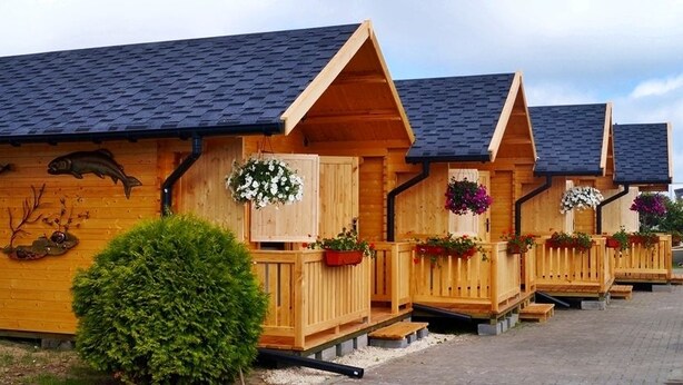 Una hilera de cabañas de madera con techos inclinados, cada una con un pequeño porche y cestas de flores.