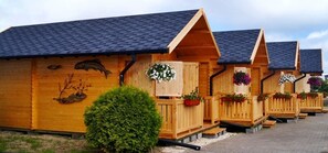 A row of wooden cabins with sloped roofs, each with a small porch and flower baskets. - Domki Onyx (Mielno)