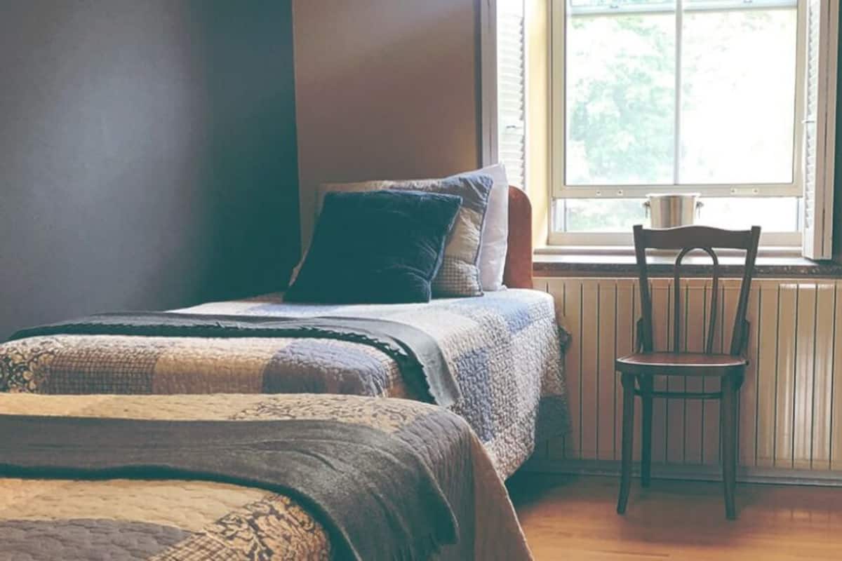 Ein Schlafzimmer mit zwei Betten, einem Sessel und einem Fenster mit Blick ins Grüne.