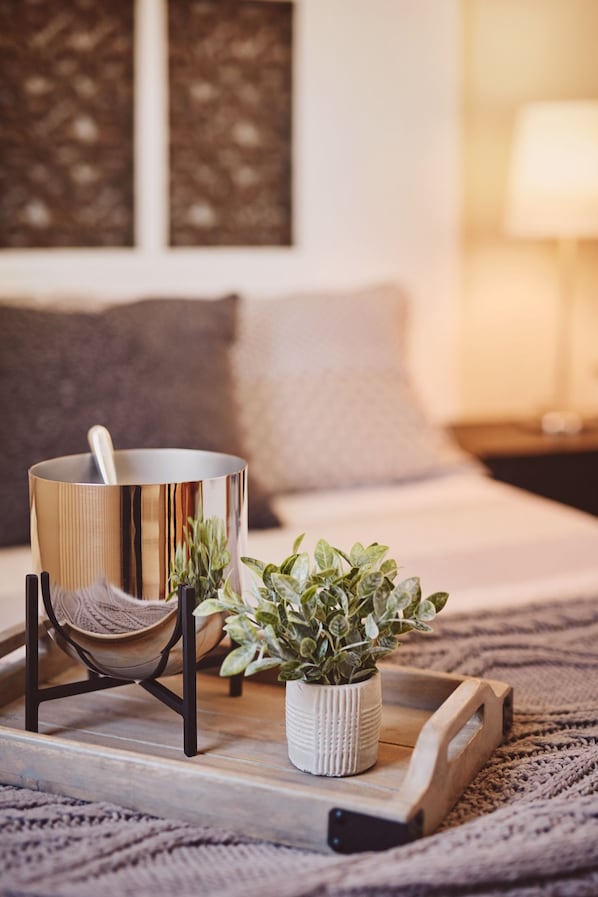Un lit avec un plateau en bois, un bol en métal, un pot blanc contenant des plantes vertes et un support noir.