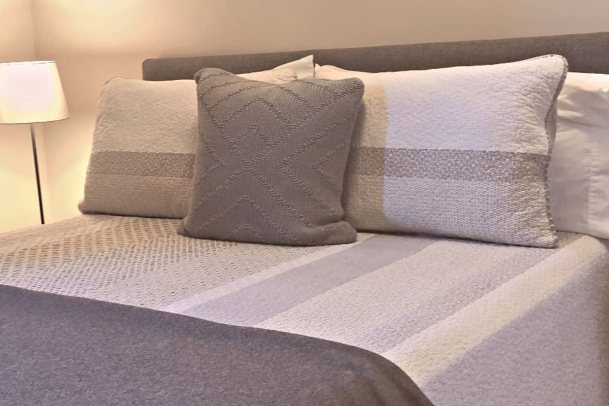 Ein Bett mit gestreifter Bettdecke und drei Kissen, eine Nachttischlampe sowie ein Nachttisch.