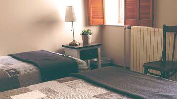 Un dormitorio con dos camas, una mesita de noche con lámpara y planta, un radiador y una silla.