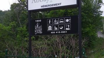 Skilt for Abbaye d'Oka med kontaktnummer og symboler der angiver faciliteter som restaurant, parkering og adgang for handicappede.
