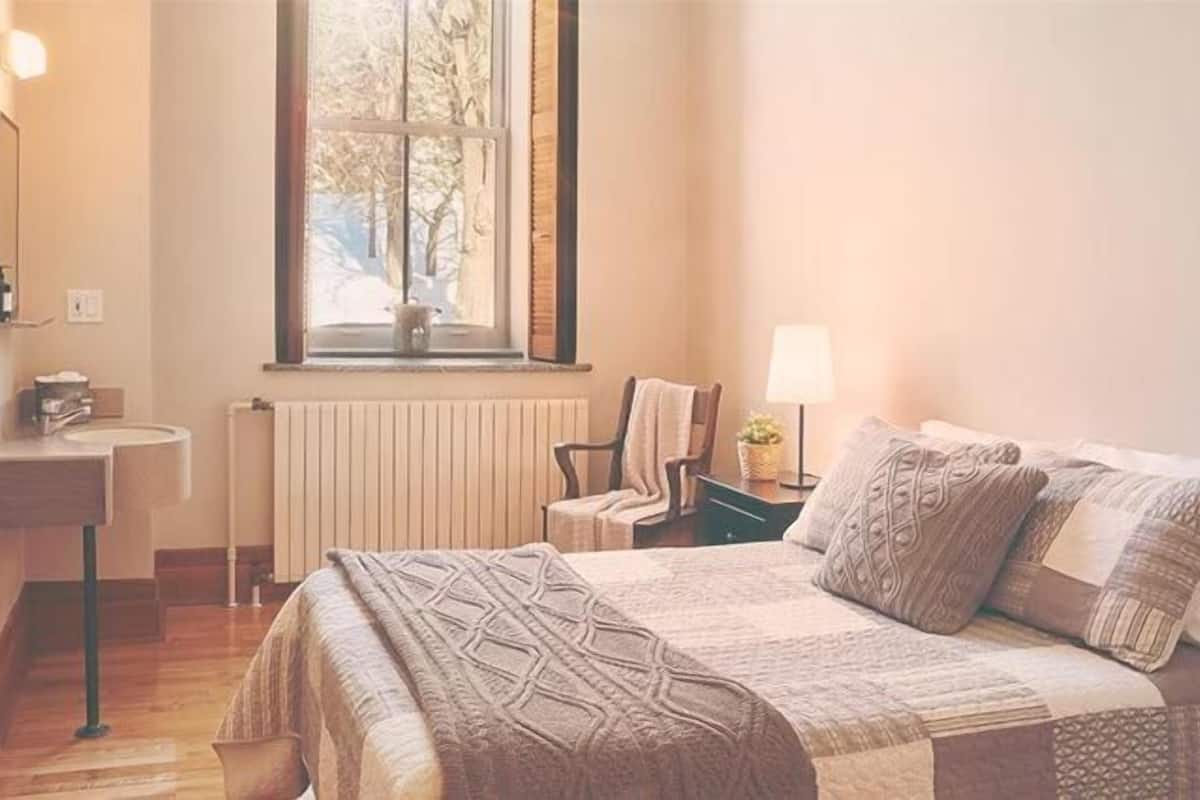 Ein Schlafzimmer mit Bett, Nachttisch, Sessel, Fenster und Heizkörper.