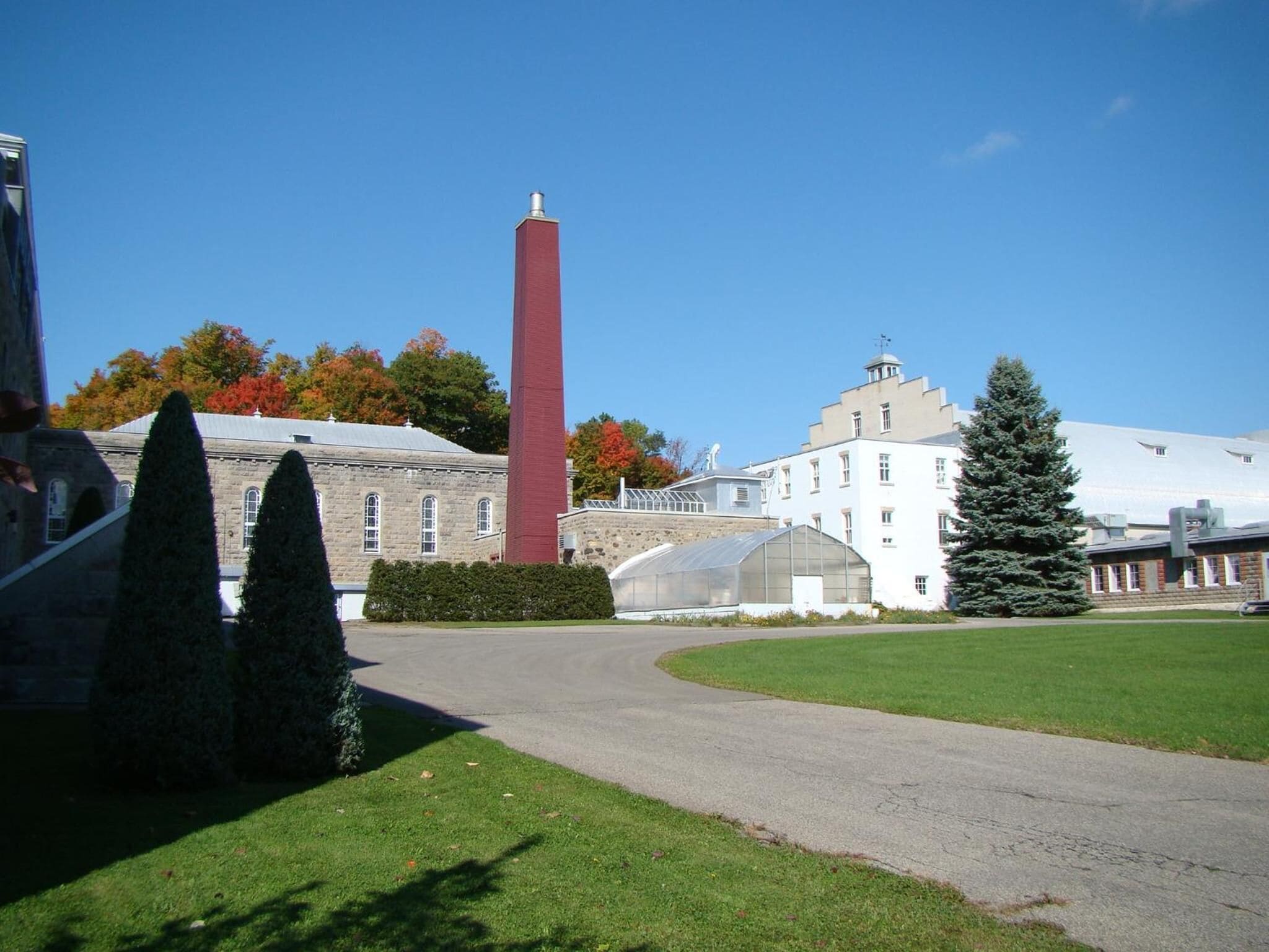 A building with a tall red chimney, a greenhouse, and a well-maintained lawn.