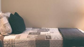 Una cama con colcha, almohadas y una mesita de noche con lámpara.