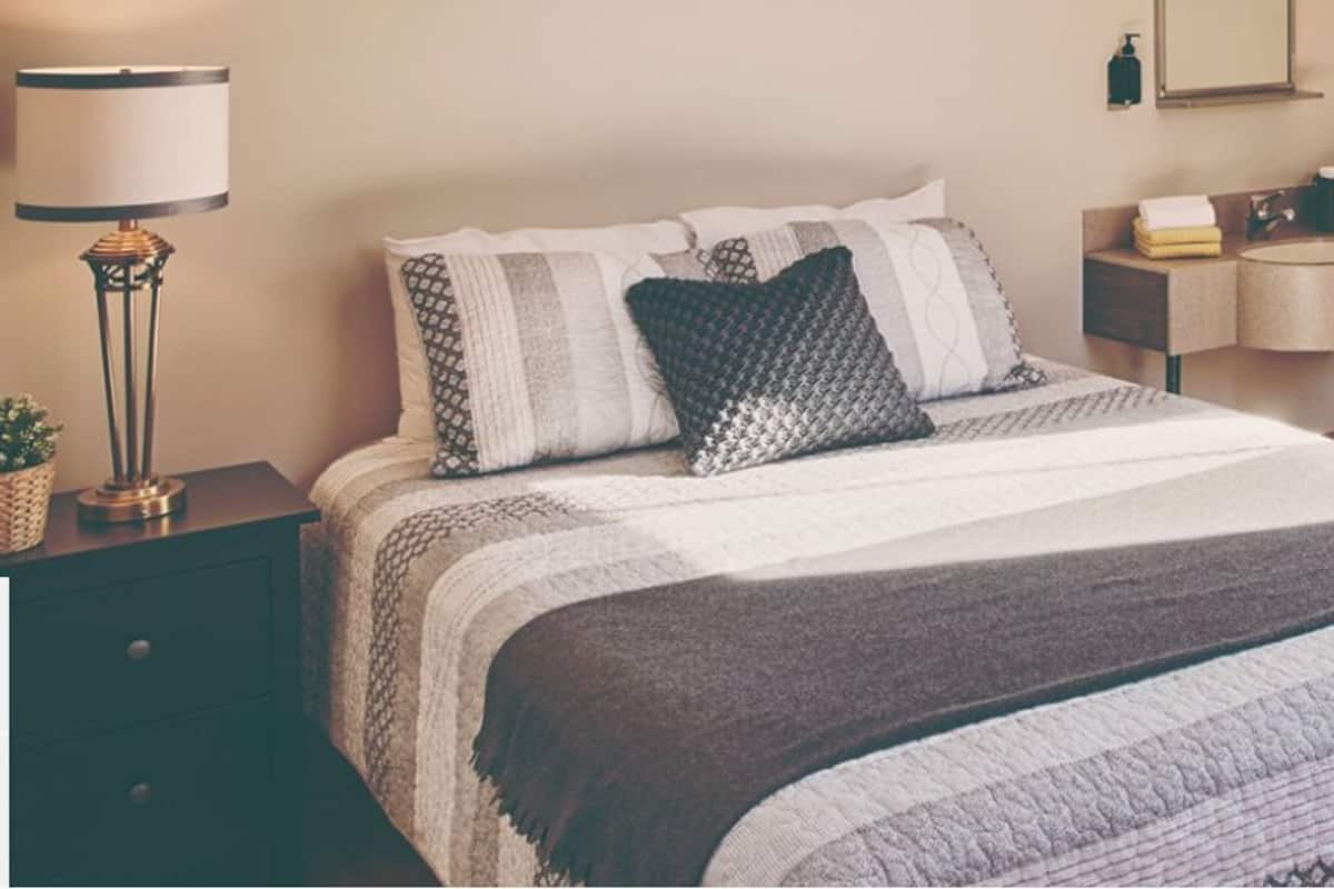Ein Schlafzimmer mit einem großen Bett, einem Nachttisch mit Lampe, einem Beistelltisch, einer Couch und einem kleinen Tisch mit Spiegel und Waschbecken.
