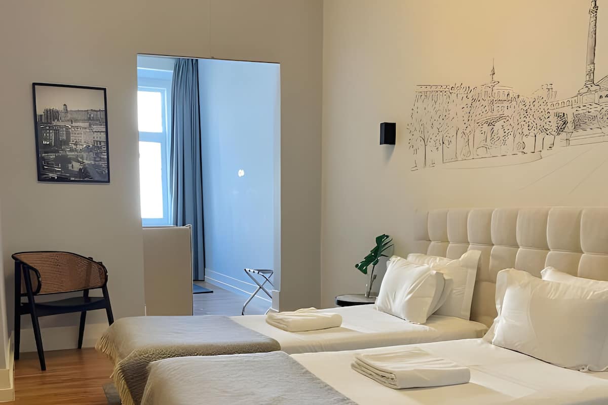 A modern hotel room with a large bed, a chair, a small table, and a cityscape wall art.