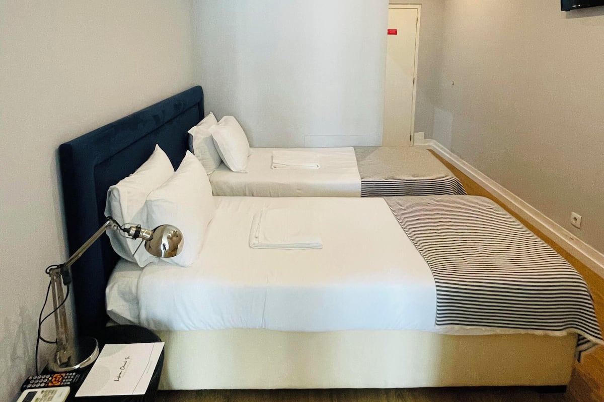 A hotel room with a large bed, a smaller bed, a TV mounted on the wall, and a bedside table with a lamp and a notepad.