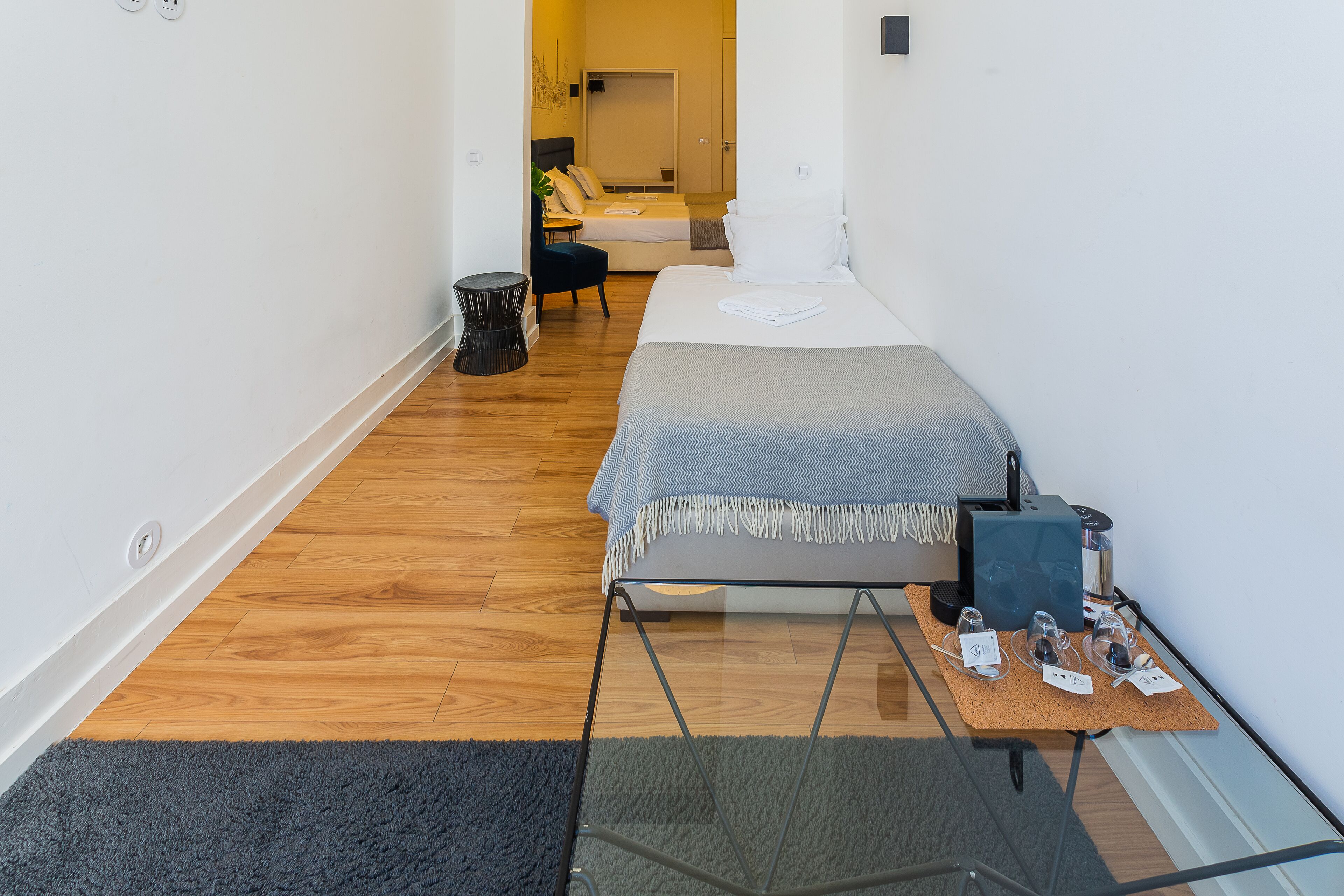 Een smalle hotelkamer met een bed, een klein tafeltje met wijnglazen en een prullenbak.