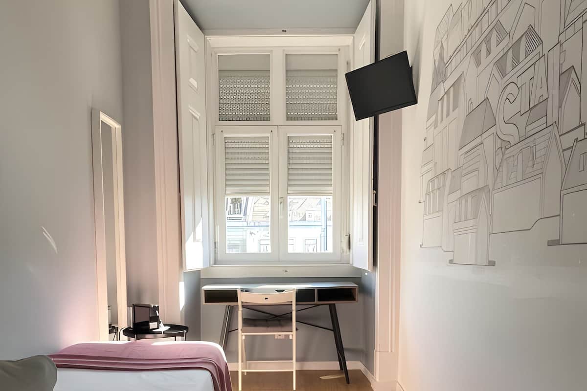 A bedroom with a bed, desk, and a wall-mounted TV.