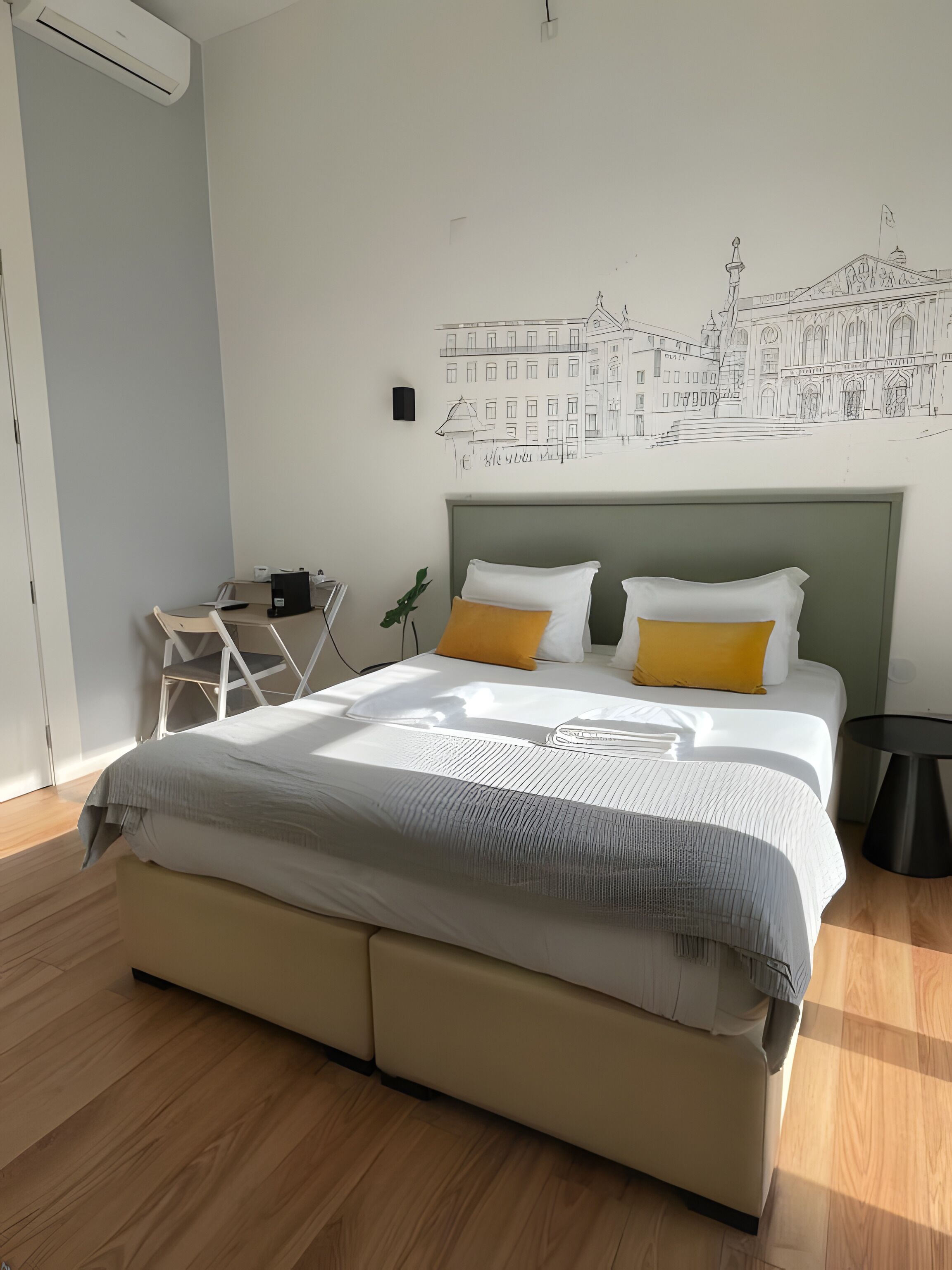 Un dormitorio con cama, escritorio, silla y una obra de arte con un edificio.