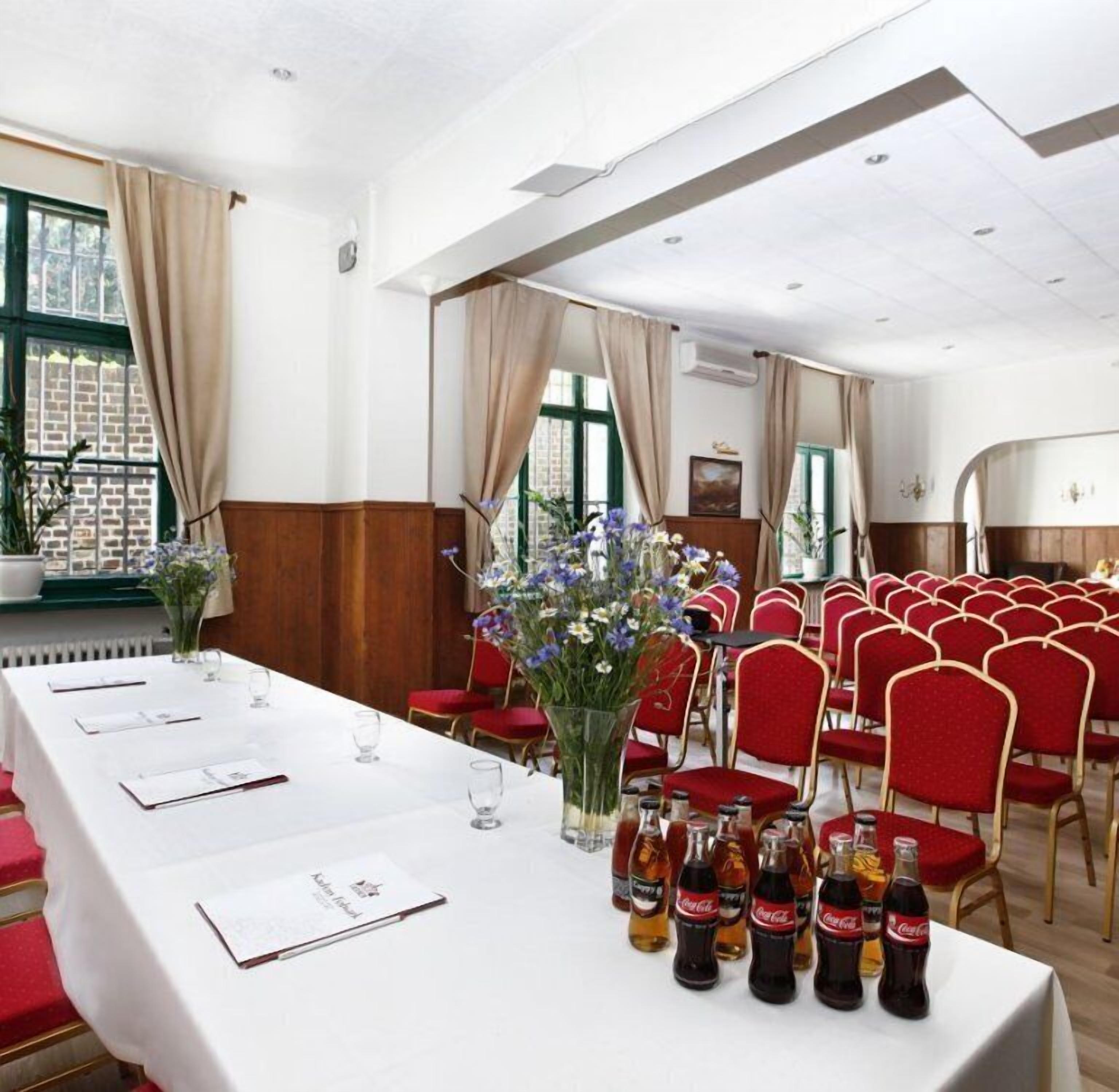 A conference room with a long table, red chairs, and floral arrangements.