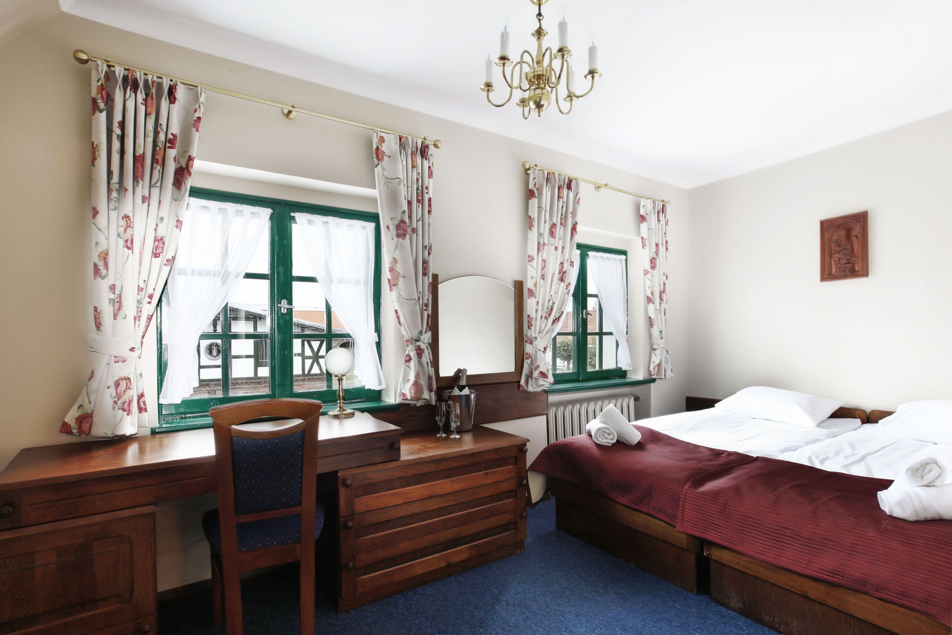 A bedroom with a wooden desk, chair, and a bed with a red blanket.