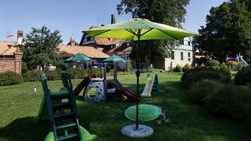 Explore a family-friendly outdoor play area with slides, climbing frames, and a shaded area under a green umbrella.