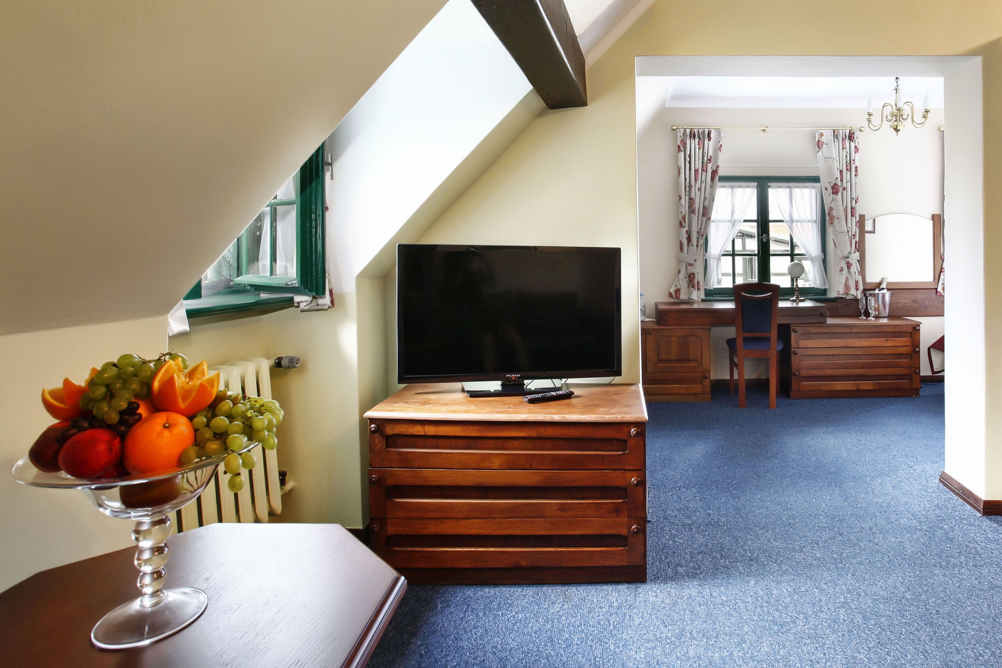 A room with a television on a wooden cabinet, a fruit bowl on a table, and a view of a dining area with a chair and a table.