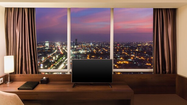 A hotel room with a large window offering a city view at dusk. - Best Western De Papilio (Surabaya)