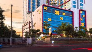 A modern high-rise building with a distinctive curved design, featuring large windows and a prominent entrance with a blue facade and yellow accents. - Best Western De Papilio (Surabaya)