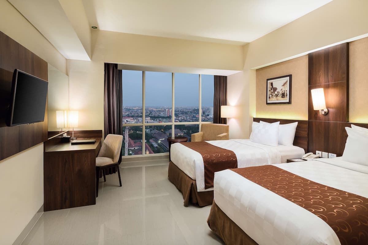 A hotel room with two beds, a desk, a chair, and a TV.