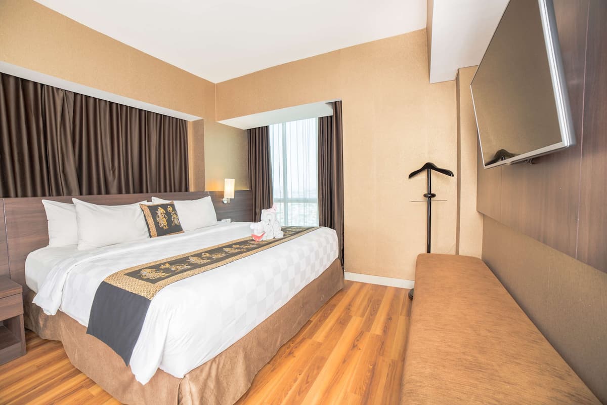 A hotel room with a large bed, a flat-screen TV mounted on the wall, and a bedside table with a lamp.