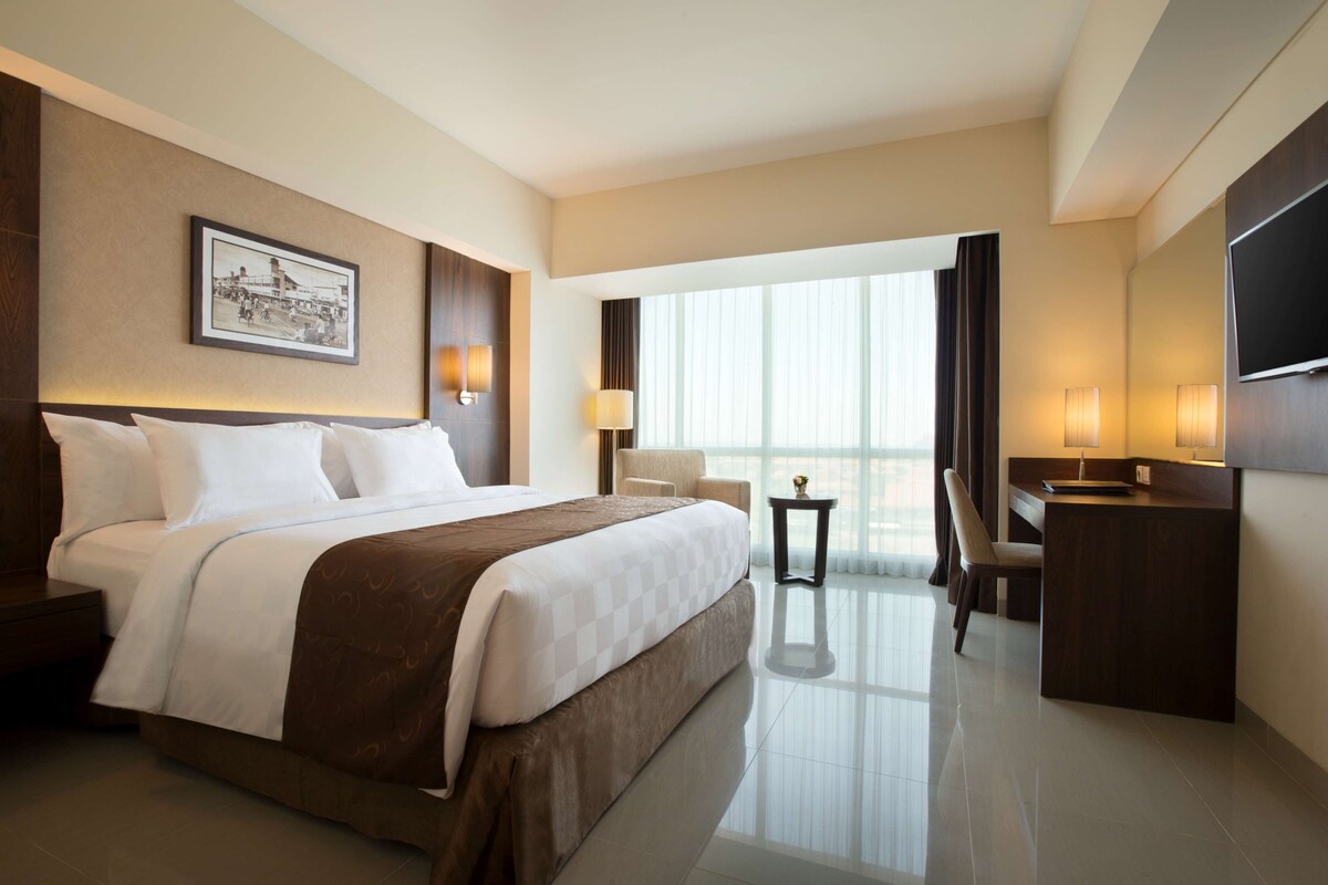 A hotel room with a large bed, a desk, a chair, a TV, and a window with curtains.