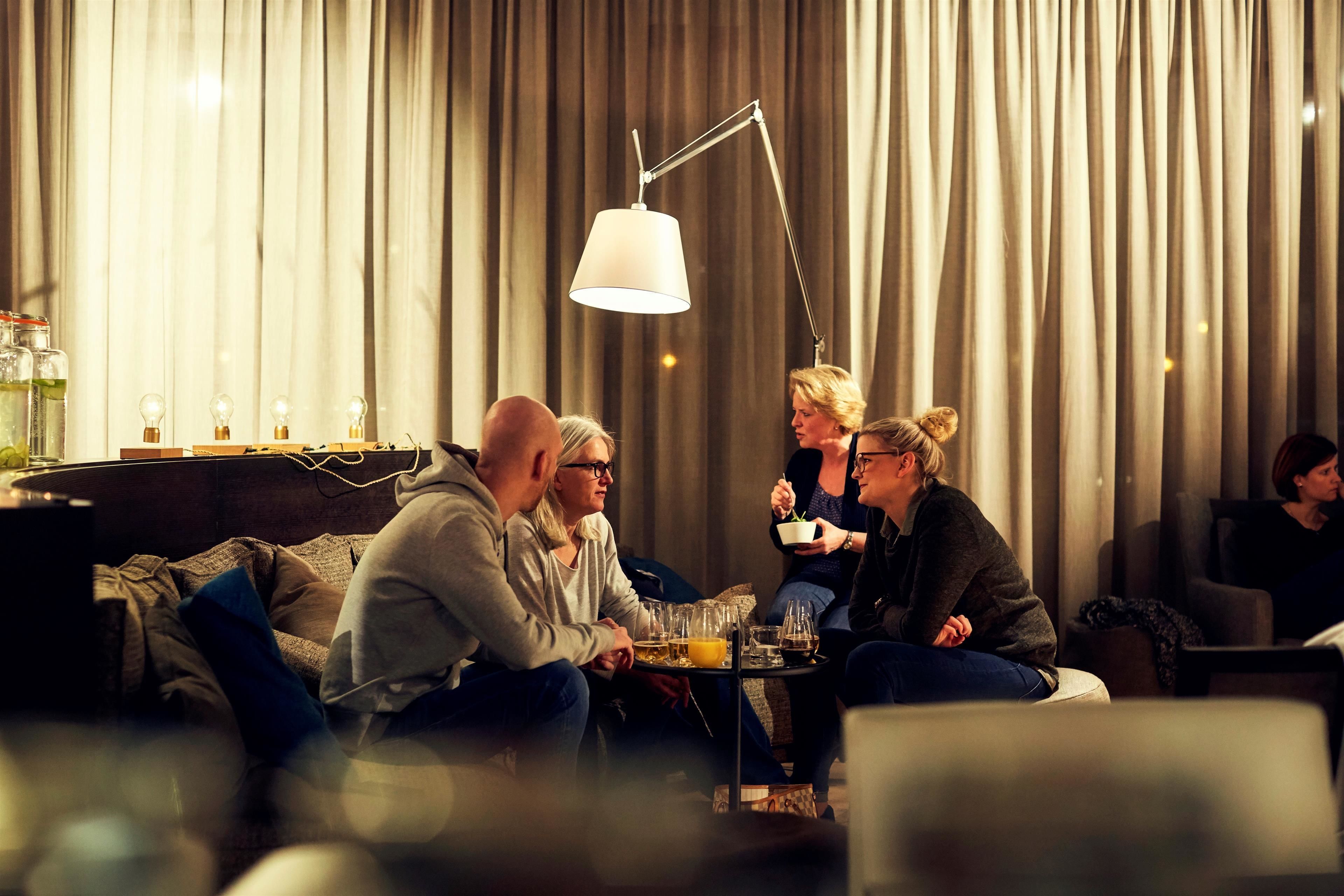 Un grupo de personas sentadas en un sofá en una habitación con poca luz, una ventana grande y cortinas.