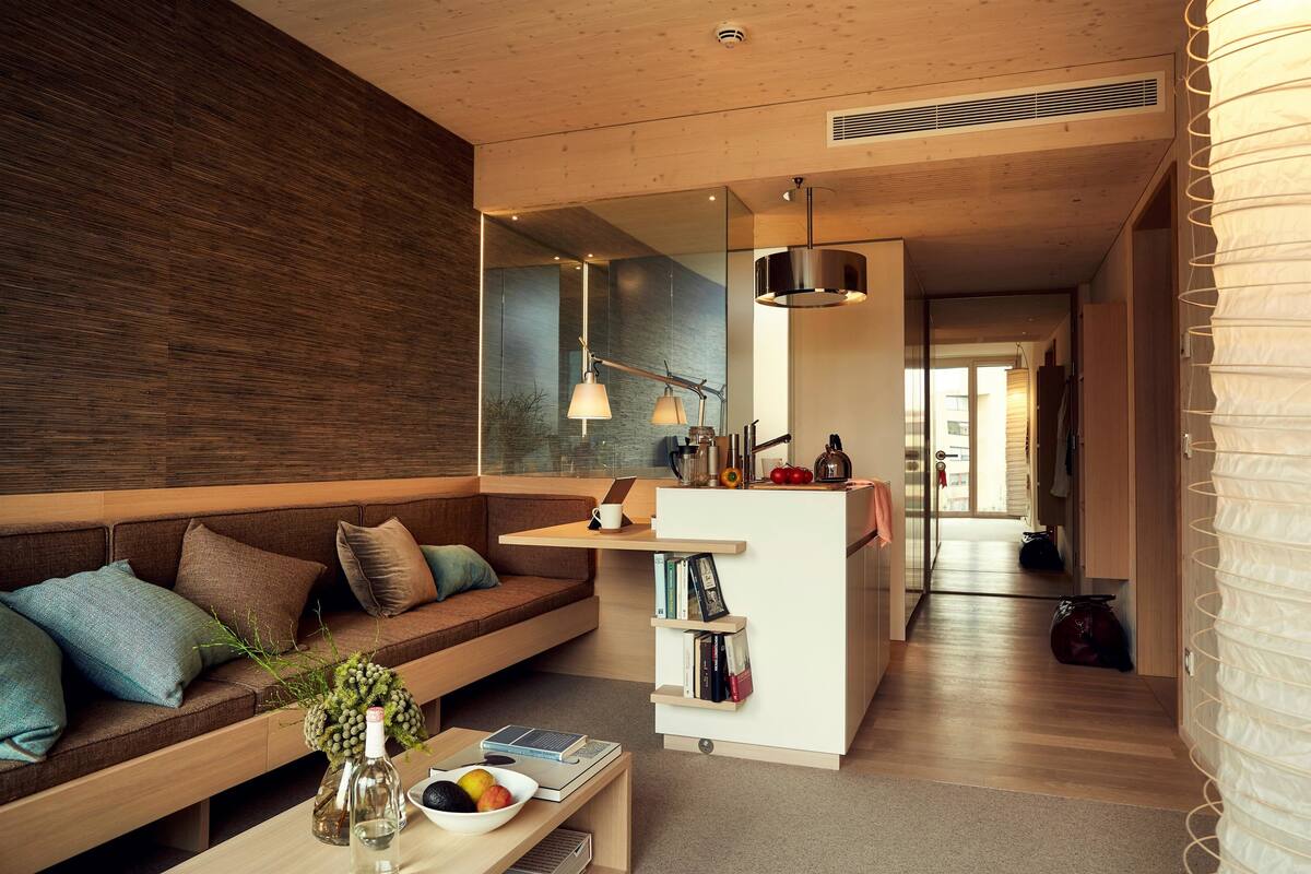 A modern living room with a wooden accent wall, a sofa with cushions, a coffee table with a bowl and books, and a small white desk with shelves.