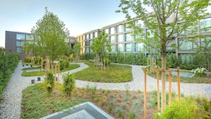 A modern building with a landscaped garden featuring pathways, trees, and various plants. - Soulmade (Garching)