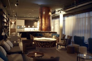 A modern living room with a central round coffee table, sofas, and armchairs arranged around it. A large copper column is a focal point, and the room has a contemporary design with a neutral color palette. - Soulmade (Garching)
