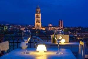 A table with two wine glasses and a lamp, overlooking a cityscape with a prominent tower. - Procurator 7 Luxury Rooms (Split)