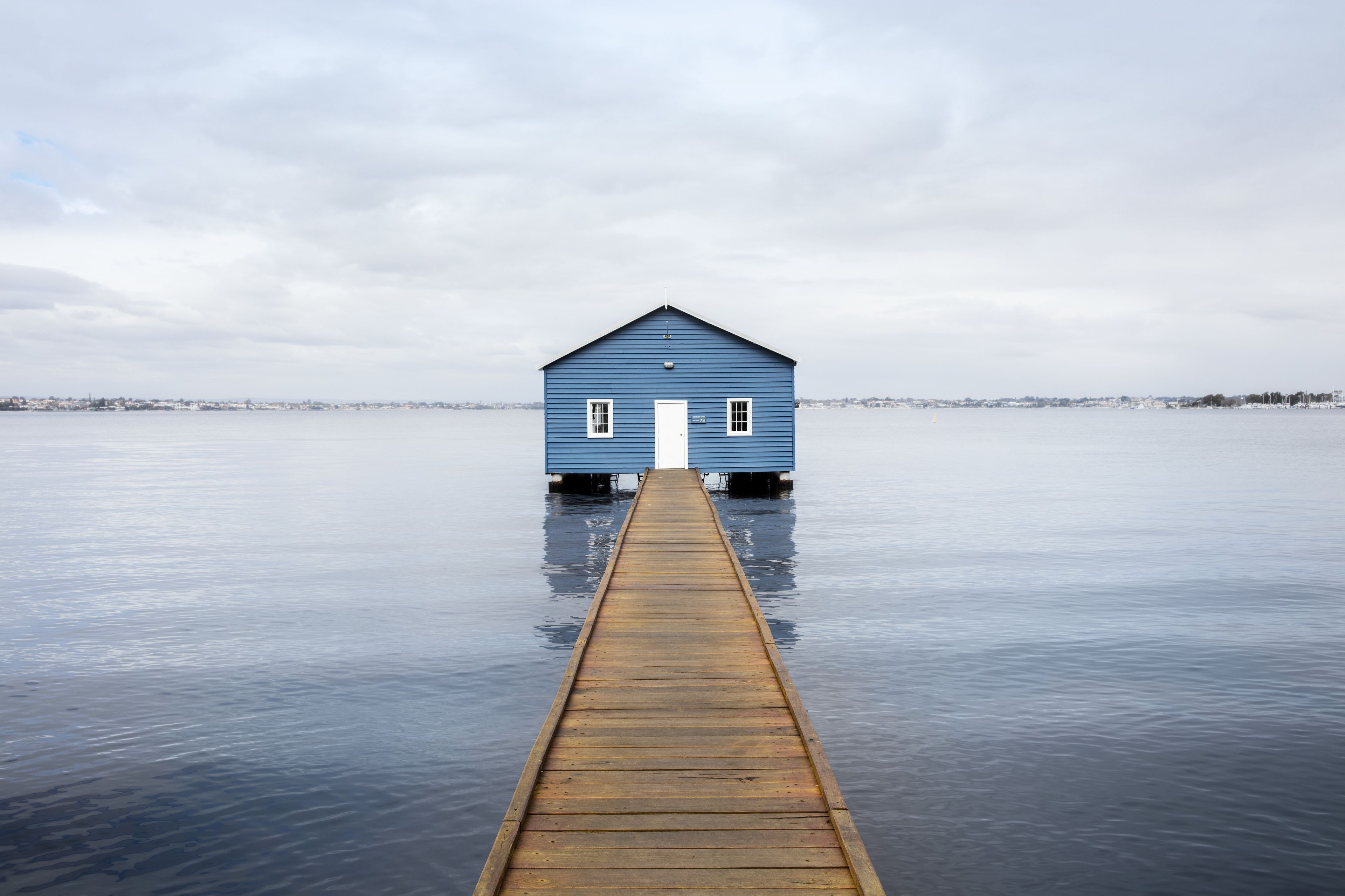 A wooden pier leading to a blue house by a calm body of water.