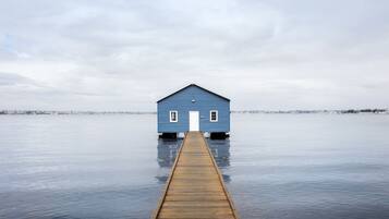 A wooden pier leading to a blue house by a calm body of water.